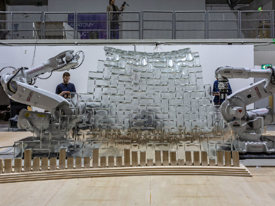 two large robotic arms putting together a glass or plastic brick wall