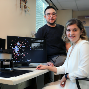 Man and women sitting at a desk with a computer screen faces us.  
